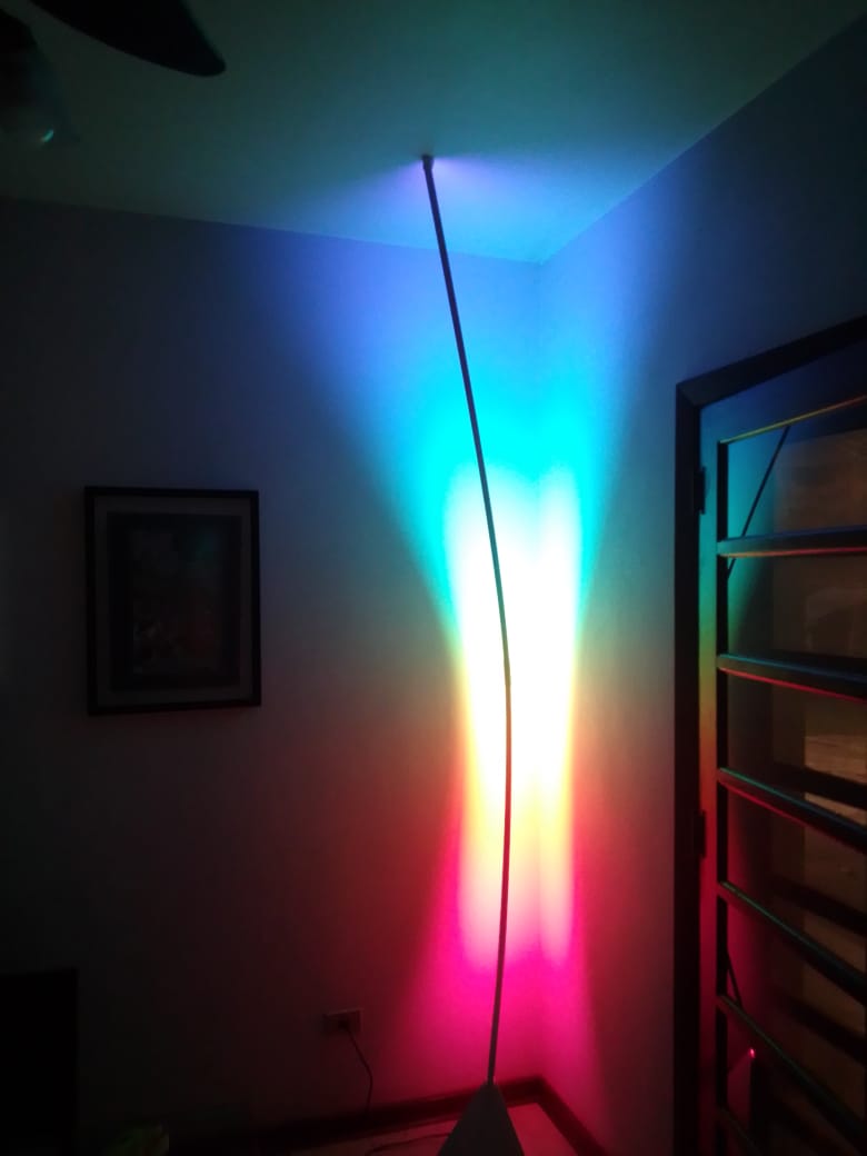 Luminária Urutau Diamond acesa no escuro, projetando um espectro de cores do chão ao teto de uma sala